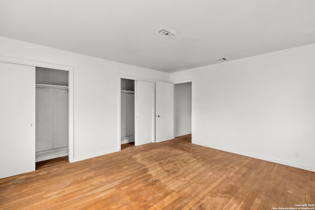 unfurnished bedroom with light hardwood / wood-style flooring and two closets