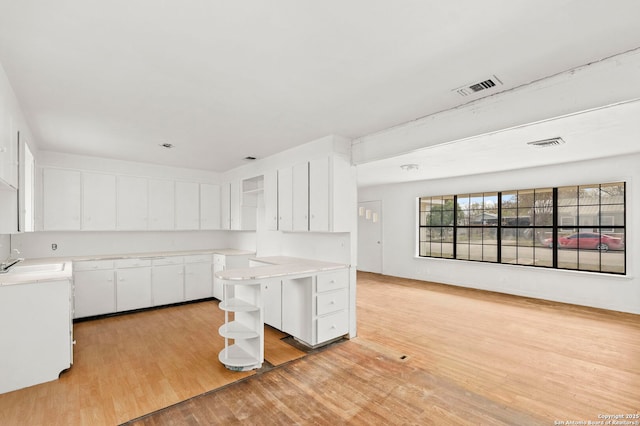 kitchen with a kitchen bar, light wood-type flooring, sink, white cabinets, and a center island