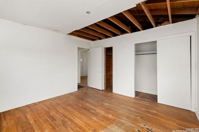 unfurnished bedroom featuring beam ceiling and hardwood / wood-style floors