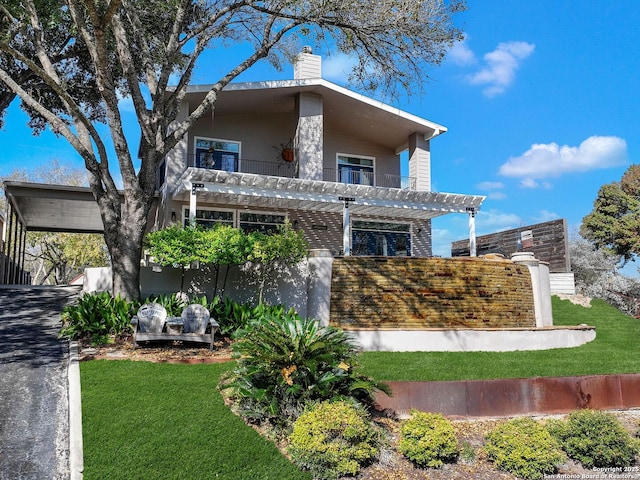 view of front of home with a balcony, a pergola, and a front lawn