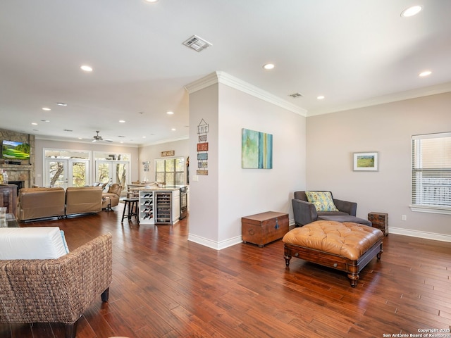 sitting room with ceiling fan, a stone fireplace, dark hardwood / wood-style flooring, and crown molding