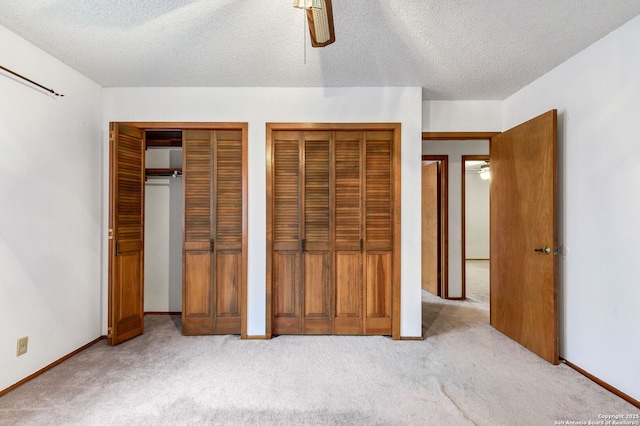 unfurnished bedroom featuring a textured ceiling, ceiling fan, light carpet, and two closets