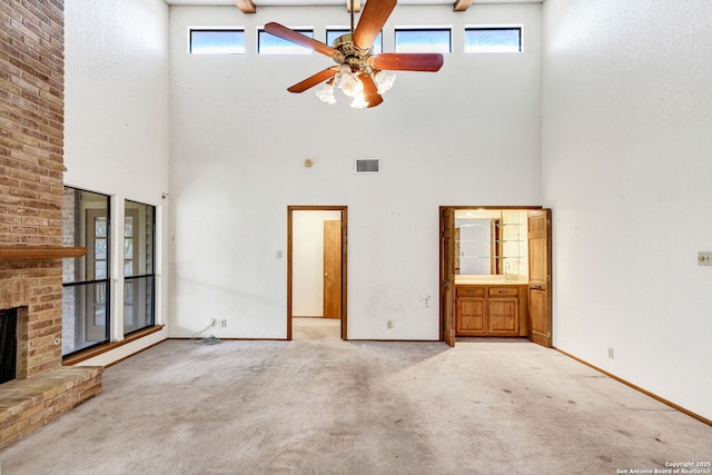 unfurnished living room featuring a brick fireplace, light carpet, a towering ceiling, and ceiling fan