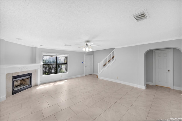 unfurnished living room featuring ceiling fan, crown molding, a textured ceiling, a fireplace, and light tile patterned flooring