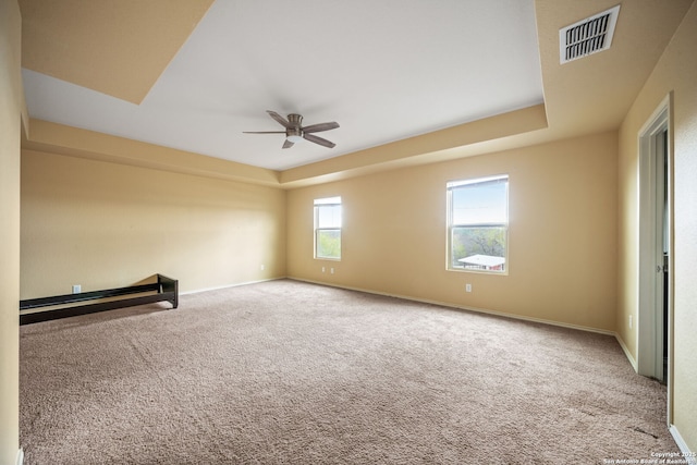 unfurnished room with a raised ceiling, ceiling fan, and carpet floors