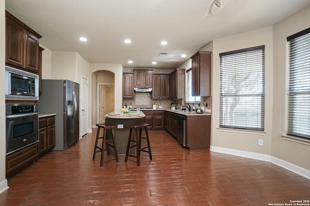 kitchen featuring a breakfast bar, decorative backsplash, dark hardwood / wood-style floors, appliances with stainless steel finishes, and a kitchen island