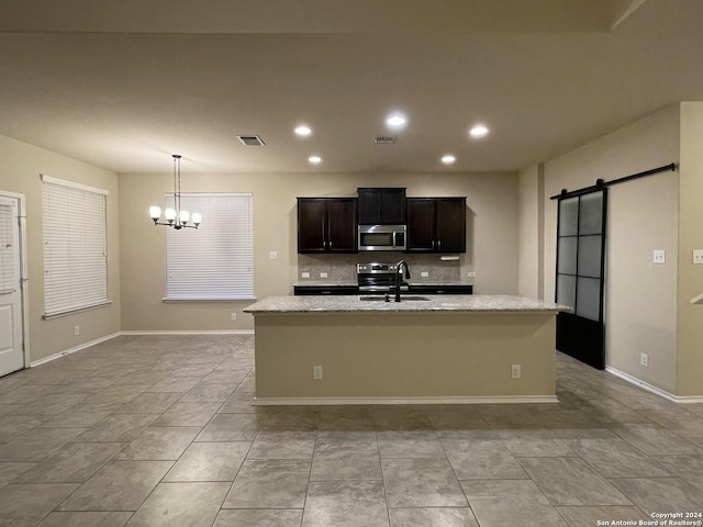 kitchen featuring sink, a barn door, an island with sink, appliances with stainless steel finishes, and light stone counters