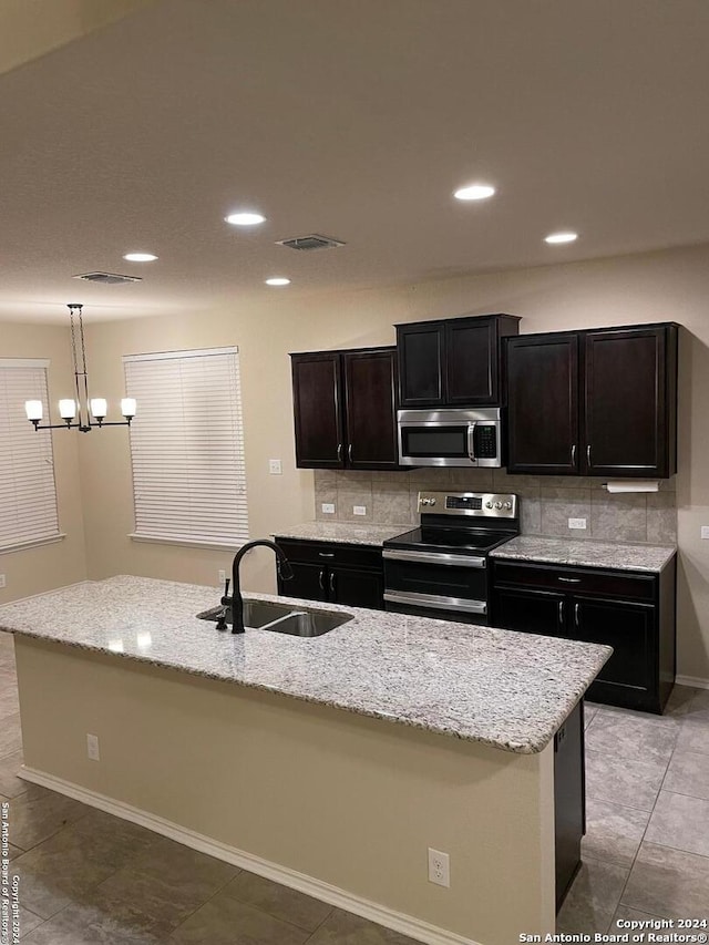 kitchen featuring decorative light fixtures, sink, stainless steel appliances, and an island with sink