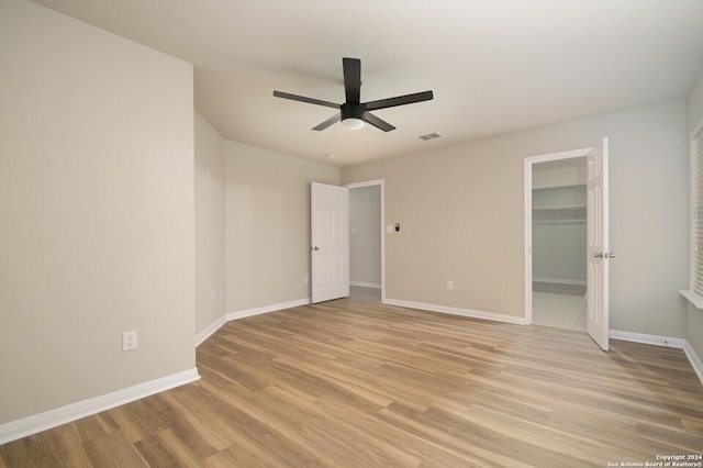 unfurnished bedroom featuring ceiling fan, a closet, a walk in closet, and light hardwood / wood-style flooring