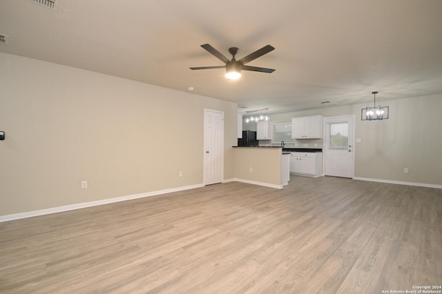 unfurnished living room featuring ceiling fan with notable chandelier and light hardwood / wood-style flooring