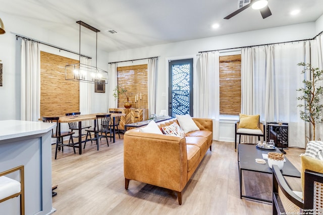 living room featuring ceiling fan with notable chandelier and light wood-type flooring