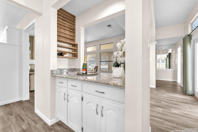 kitchen featuring white cabinets, light stone countertops, and light hardwood / wood-style flooring