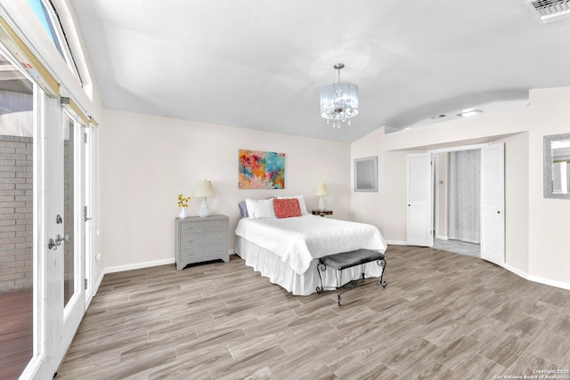 bedroom with ensuite bath, an inviting chandelier, light hardwood / wood-style flooring, and vaulted ceiling