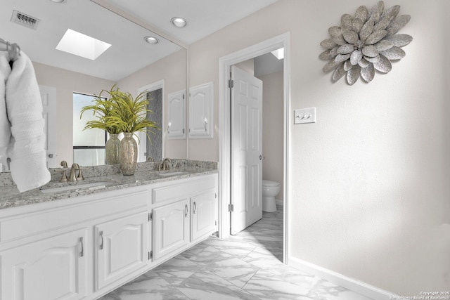 bathroom with a skylight, vanity, and toilet