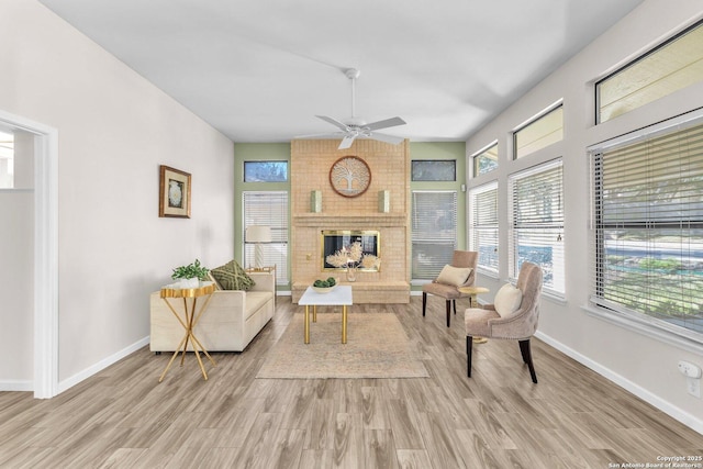 living area featuring a brick fireplace, light hardwood / wood-style flooring, and ceiling fan