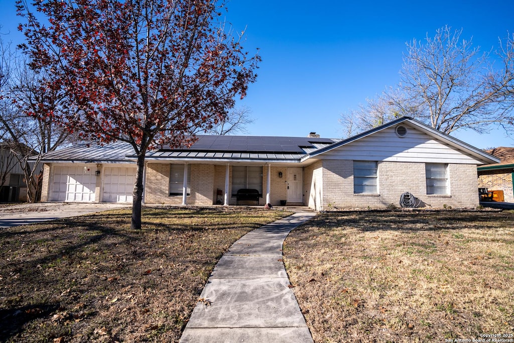 ranch-style home featuring a front yard, a garage, solar panels, and a porch