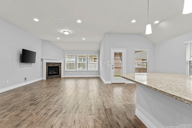 unfurnished living room with lofted ceiling, a stone fireplace, and dark wood-type flooring