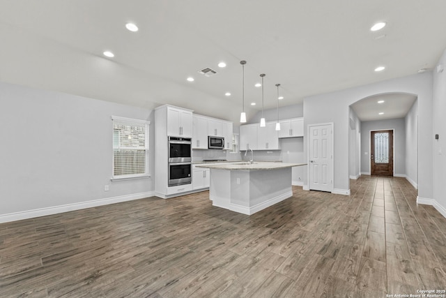 kitchen with hardwood / wood-style floors, pendant lighting, a center island with sink, white cabinets, and appliances with stainless steel finishes