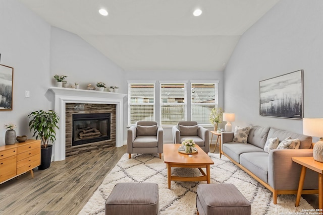 living room featuring a stone fireplace, light hardwood / wood-style floors, and lofted ceiling