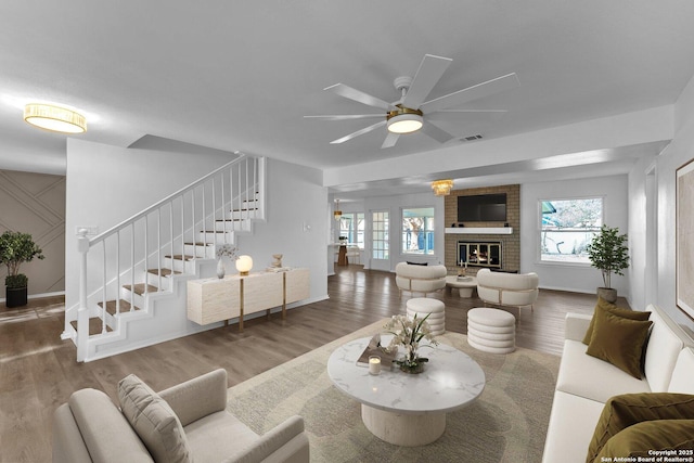 living room featuring plenty of natural light, ceiling fan, wood-type flooring, and a brick fireplace