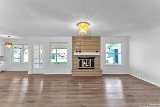 unfurnished living room featuring a chandelier, dark hardwood / wood-style flooring, and a brick fireplace