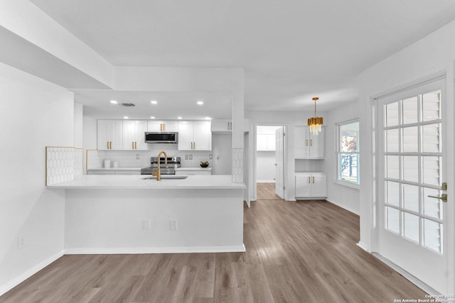 kitchen featuring kitchen peninsula, stainless steel appliances, sink, decorative light fixtures, and white cabinetry