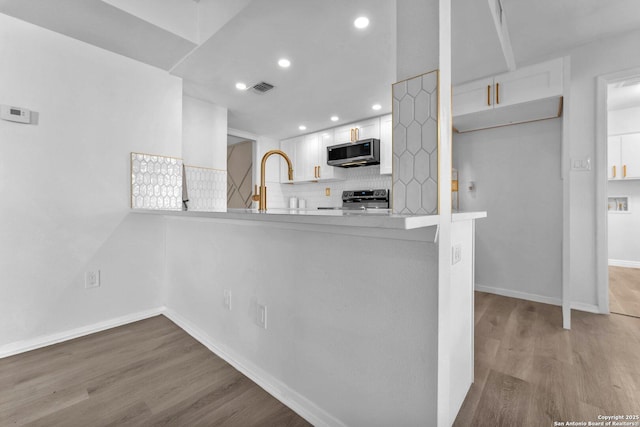 kitchen with white cabinetry, stainless steel appliances, backsplash, kitchen peninsula, and light hardwood / wood-style floors