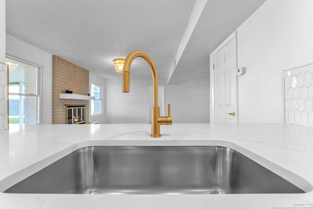 room details featuring light stone countertops, a brick fireplace, and sink