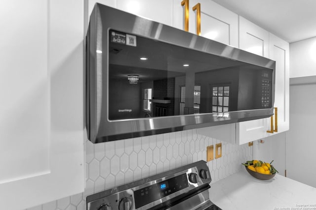 room details featuring white cabinets, decorative backsplash, and range