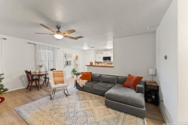 living room with light hardwood / wood-style floors, a textured ceiling, and ceiling fan