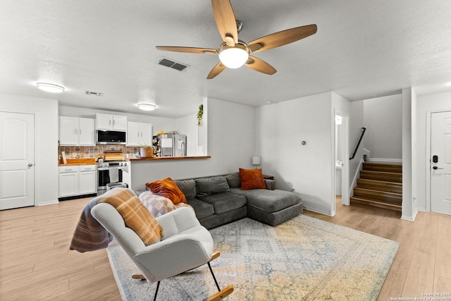 living room with a textured ceiling, ceiling fan, and light hardwood / wood-style floors