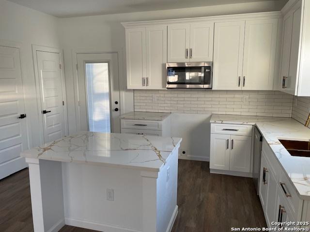 kitchen with tasteful backsplash, light stone counters, a center island, and white cabinets