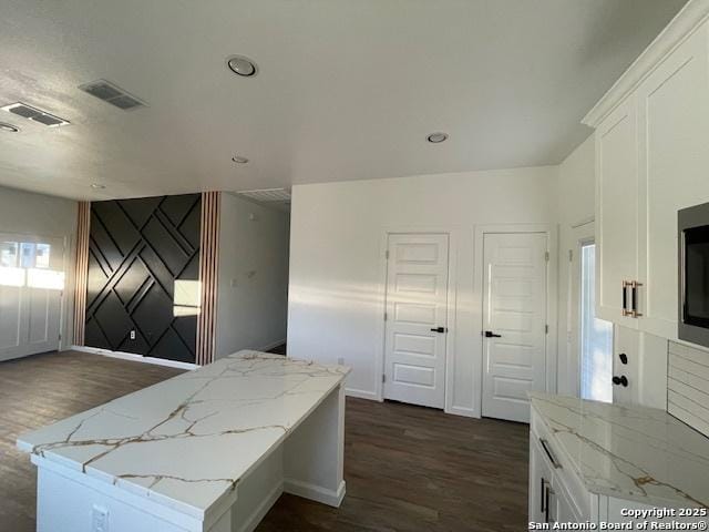 kitchen with dark hardwood / wood-style flooring, light stone countertops, a center island, and white cabinets