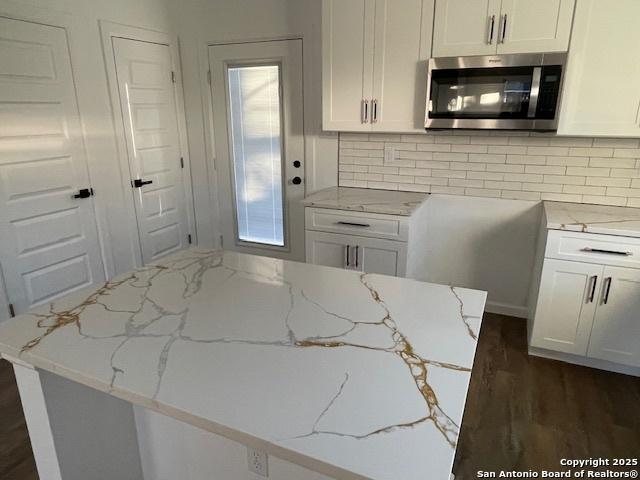 kitchen with tasteful backsplash, white cabinetry, dark wood-type flooring, and light stone counters