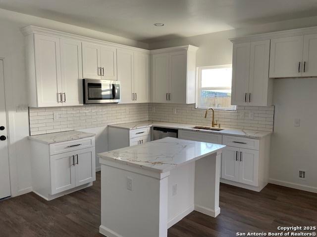 kitchen featuring sink, stainless steel appliances, a kitchen island, light stone counters, and white cabinets