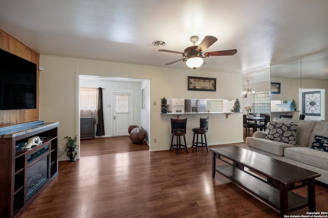 living room with ceiling fan with notable chandelier, dark hardwood / wood-style flooring, and wooden walls