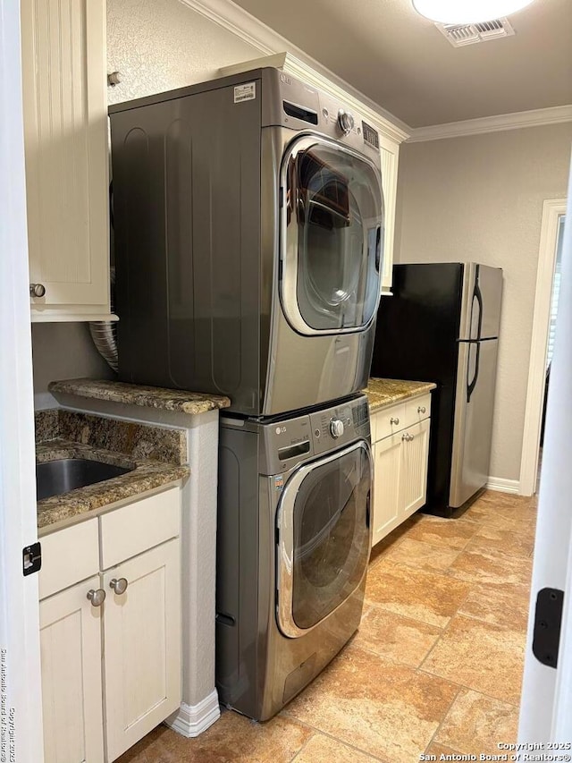 laundry area featuring stacked washer and dryer, cabinets, and ornamental molding