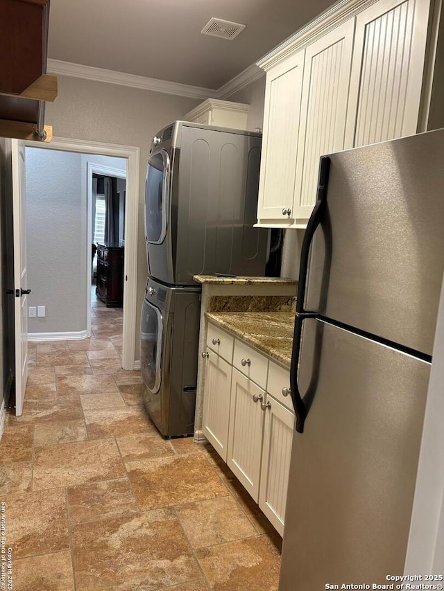 kitchen with stone countertops, crown molding, stainless steel fridge, stacked washer / drying machine, and white cabinetry