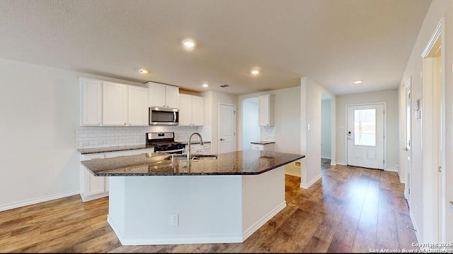 kitchen with white cabinets, dark stone countertops, an island with sink, and appliances with stainless steel finishes