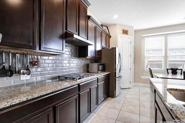 kitchen with light stone countertops, backsplash, dark brown cabinetry, stainless steel appliances, and light tile patterned flooring