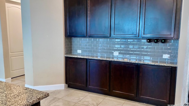 kitchen featuring backsplash, light stone countertops, dark brown cabinets, and light tile patterned floors