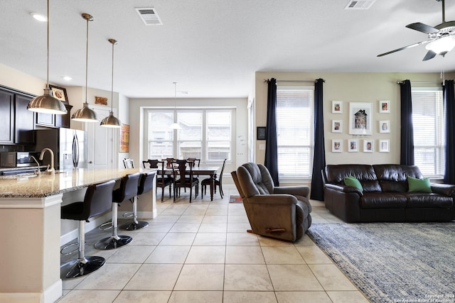 living room featuring ceiling fan, sink, light tile patterned floors, and a textured ceiling