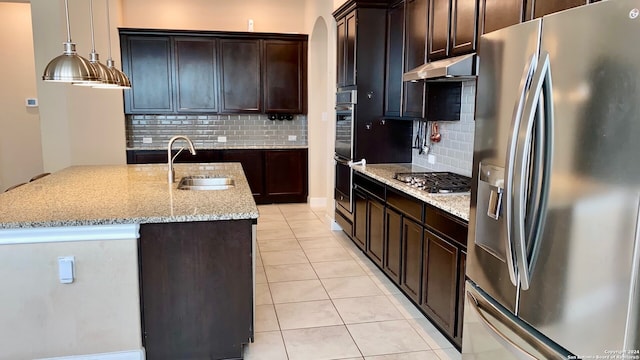 kitchen with a kitchen island with sink, sink, hanging light fixtures, light stone counters, and stainless steel appliances