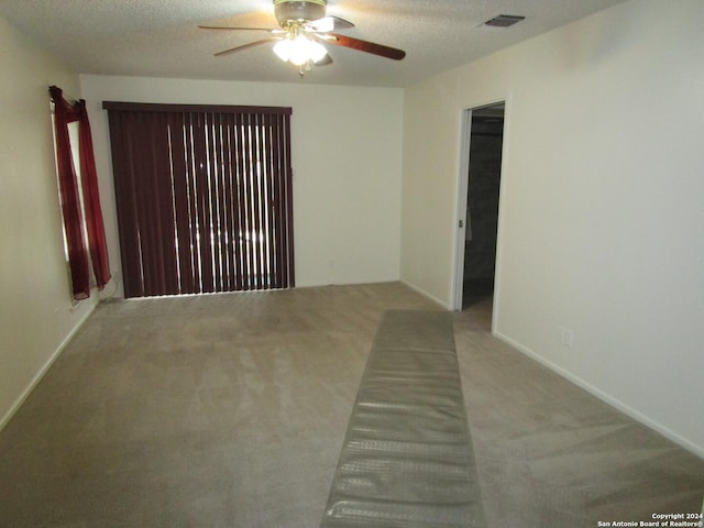 spare room with a textured ceiling, light colored carpet, and ceiling fan