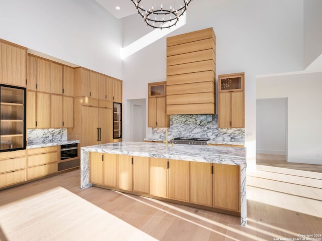 kitchen with a chandelier, a high ceiling, light brown cabinets, and backsplash