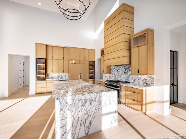 kitchen featuring light stone counters, high end stove, backsplash, a towering ceiling, and a center island with sink