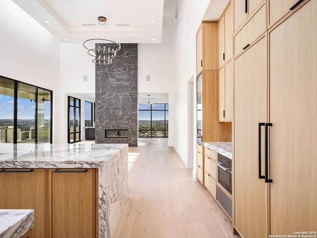 kitchen featuring a fireplace, light stone counters, light brown cabinetry, and a chandelier