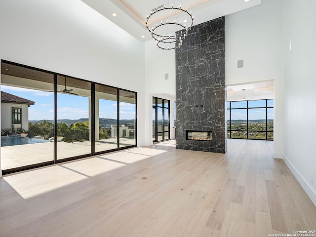 unfurnished living room featuring a premium fireplace, ceiling fan with notable chandelier, light hardwood / wood-style floors, and a high ceiling