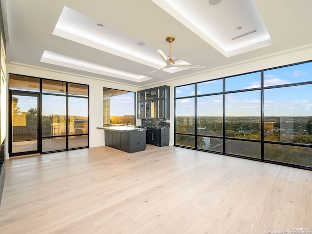 unfurnished living room featuring light wood-type flooring, a tray ceiling, plenty of natural light, and a wall of windows