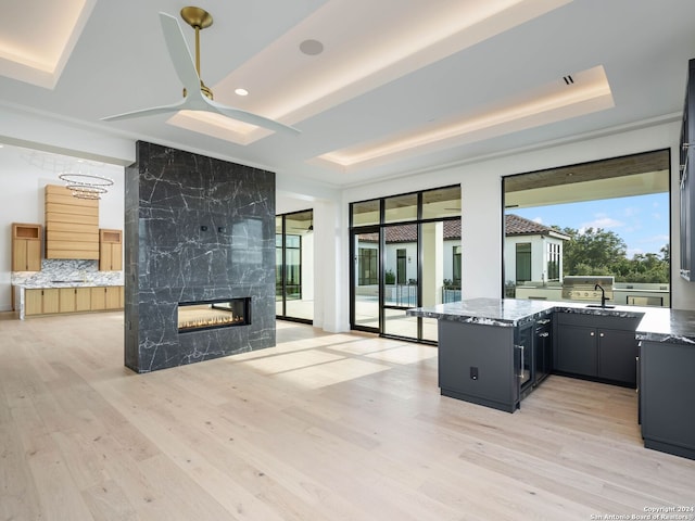 unfurnished living room featuring a tray ceiling, ceiling fan, a high end fireplace, and light wood-type flooring